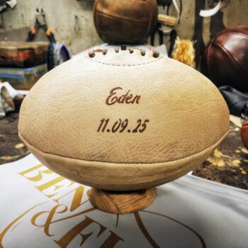 Ballon de rugby en cuir crème personnalisé avec un prénom et une date gravés dans la police Bassy. Ce modèle Ben & Flo est entièrement fabriqué à la main en France, à partir de cuir naturel sans patine, dont la teinte évolue vers un ton miel au fil du temps. Idéal comme cadeau de naissance, souvenir de club ou décoration vintage sur-mesure dans l’esprit du rugby authentique.