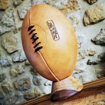 Ballon de rugby en cuir crème naturel, fabriqué à la main dans l’atelier Ben & Flo en France. Ce modèle 4 panneaux, sans patine ajoutée, présente une teinte claire et lumineuse qui se réchauffe naturellement avec le temps. Posé sur un socle en bois clair, il incarne l’élégance du rugby vintage et la beauté du cuir vivant. Idéal en décoration ou en cadeau rugby personnalisé.