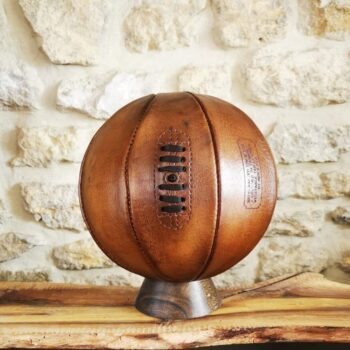 Ballon de basket en cuir vintage couleur miel exposé sur socle en bois massif
