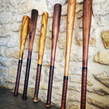 Miniature vidéo présentant six battes de baseball en bois vintage avec poignées en cuir, adossées à un mur en pierre.