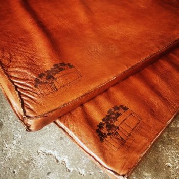 Deux tapis de gym en cuir marron avec gravure personnalisée d'un logo, détail des finitions et des coutures.