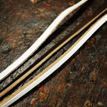 Lacets plats en cuir blanc et marron présentés sur un plan de travail, comparant les deux couleurs disponibles pour réparer un ballon de foot US ou restaurer un gant de boxe.