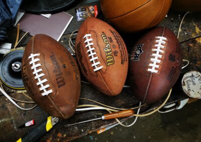 Collection de ballons de football américain vintage restaurés avec des lacets en cuir blanc et marron, montrant le rendu final après réparation.
