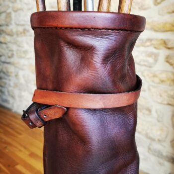 Partie supérieure d'un sac de golf en cuir brun vintage, avec bordure cousue, sangle et manches de clubs anciens en bois.