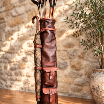 Sac de golf en cuir brun vintage avec clubs anciens en bois et parapluie à carreaux fixé sur le côté.