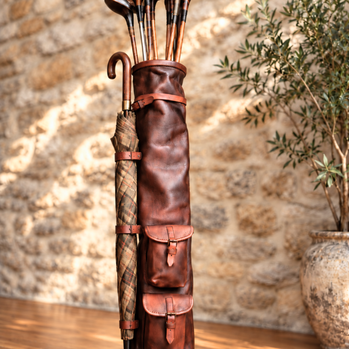 Sac de golf en cuir brun vintage avec clubs anciens en bois et parapluie à carreaux fixé sur le côté.
