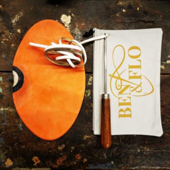 Kit de réparation complet pour ballon de football américain Ben & Flo, présenté sur fond cuir orange. L’ensemble comprend une vessie en latex naturel, un lacet en cuir, une aiguille de laçage professionnelle en bois et acier, et une housse de rangement en coton avec logo Ben & Flo. Conçu pour les clubs, ateliers et passionnés de sport vintage.