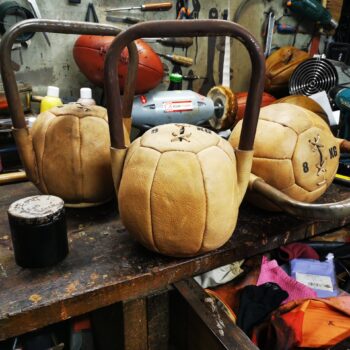 Kettlebell vintage en cuir fabriqué à la main dans l’atelier Ben & Flo, avec medecine balls en arrière-plan.