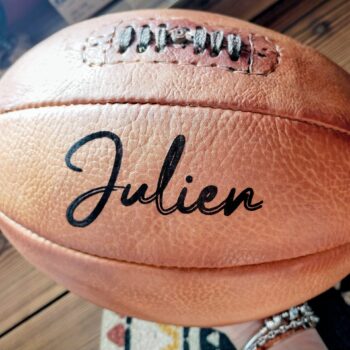 Ballon de rugby vintage personnalisé avec gravure du prénom “Julien” en police Bassy, cuir honey patiné à la main par Ben & Flo, idéal pour un cadeau unique à un coach de rugby.