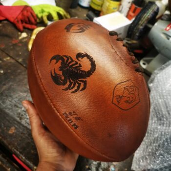 Ballon de rugby en cuir personnalisé avec plusieurs logos gravés, préparé dans l’atelier Ben & Flo. L'accompagnment pour personnalisation sur-mesure a été nécessaire.
