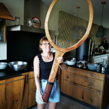 Femme tenant une raquette tennis XXL en bois dans une cuisine