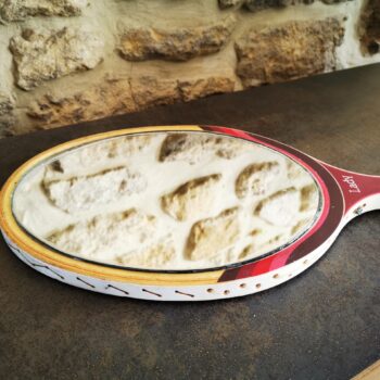 Gros plan sur un miroir inséré dans une raquette de tennis vintage avec fond pierre