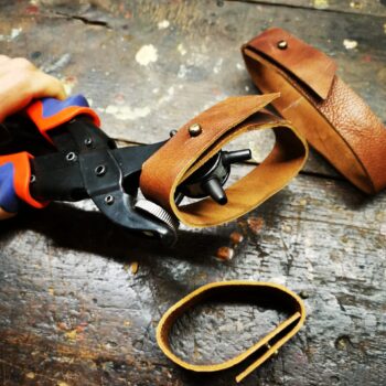 Fabrication artisanale d’un support mural pour batte de baseball, sangle en cuir, boucle et outils posés sur un établi.