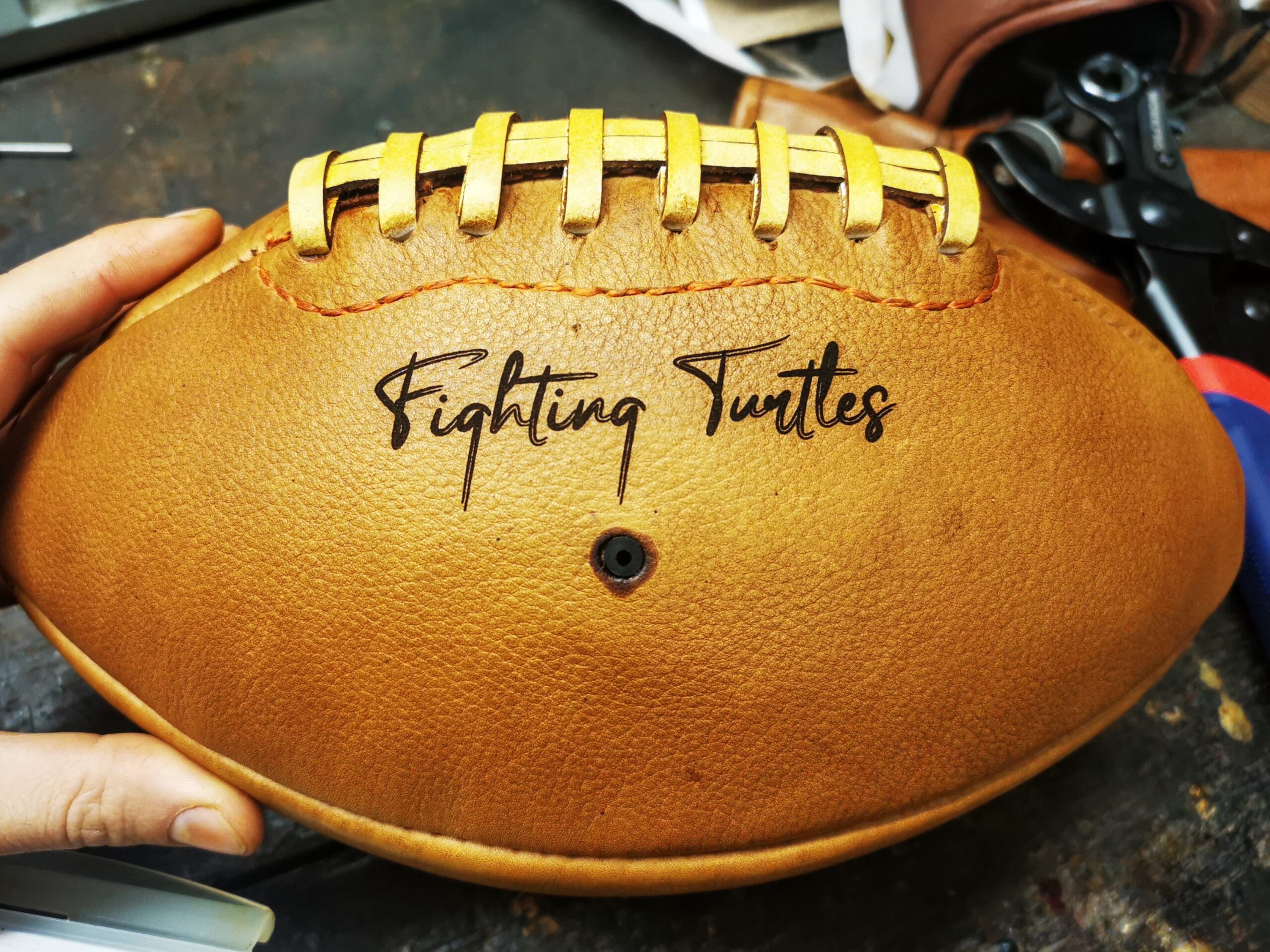 Ballon de foot américain vintage en cuir patiné avec une gravure texte “Fighting Turtles”, réalisé dans notre atelier. La couture centrale et la teinte miel offrent un style rétro recherché, parfait pour une décoration football américain ou pour offrir un cadeau sportif personnalisé. Idéal pour fans de football US, clubs ou collectors.