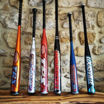 Plusieurs battes de baseball en aluminium alignées devant un mur en pierre.