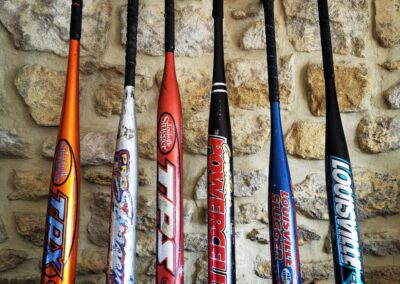 Plusieurs battes de baseball en aluminium alignées devant un mur en pierre.