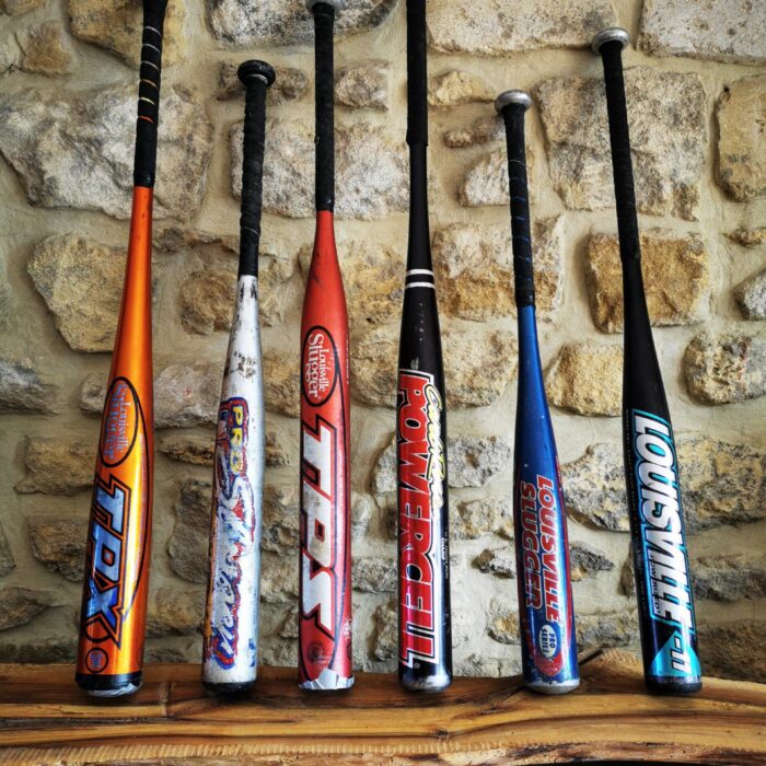 Plusieurs battes de baseball en aluminium alignées devant un mur en pierre.