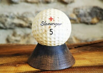Balle de golf posée sur un mini socle foncé en chêne