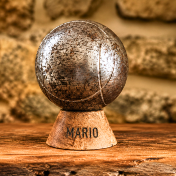 Socle boule de pétanque en bois personnalisé avec gravure MARIO et boule ancienne exposée sur une table en bois