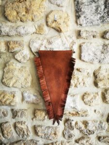 Fanion en cuir marron avec franges suspendu sur un mur en pierre