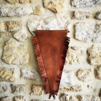 Fanion en cuir marron avec franges suspendu sur un mur en pierre
