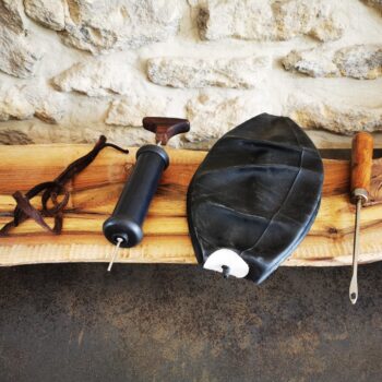 Kit complet de réparation pour ballon de basket ancien à lacets avec vessie en butyle, petite pompe manuelle avec aiguille, lacet marron et passe-lacet en acier avec manche en bois, présenté sur un établi.