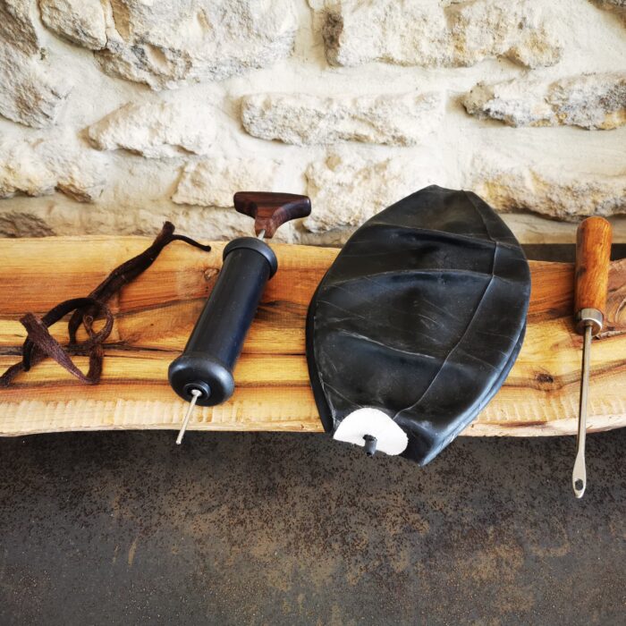 Kit complet de réparation pour ballon de basket ancien à lacets avec vessie en butyle, petite pompe manuelle avec aiguille, lacet marron et passe-lacet en acier avec manche en bois, présenté sur un établi.