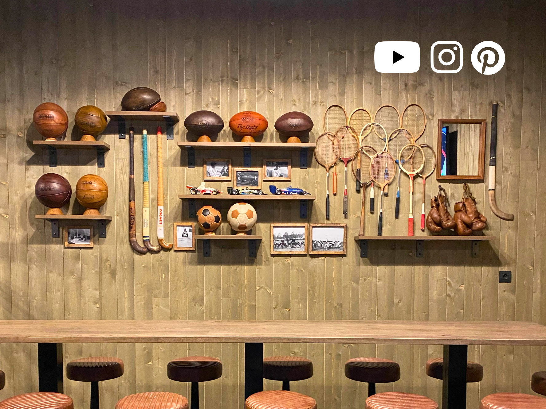 Mur décoratif avec ballons en cuir vintage, anciennes raquettes, gants de boxe et logos YouTube, Instagram et Pinterest.