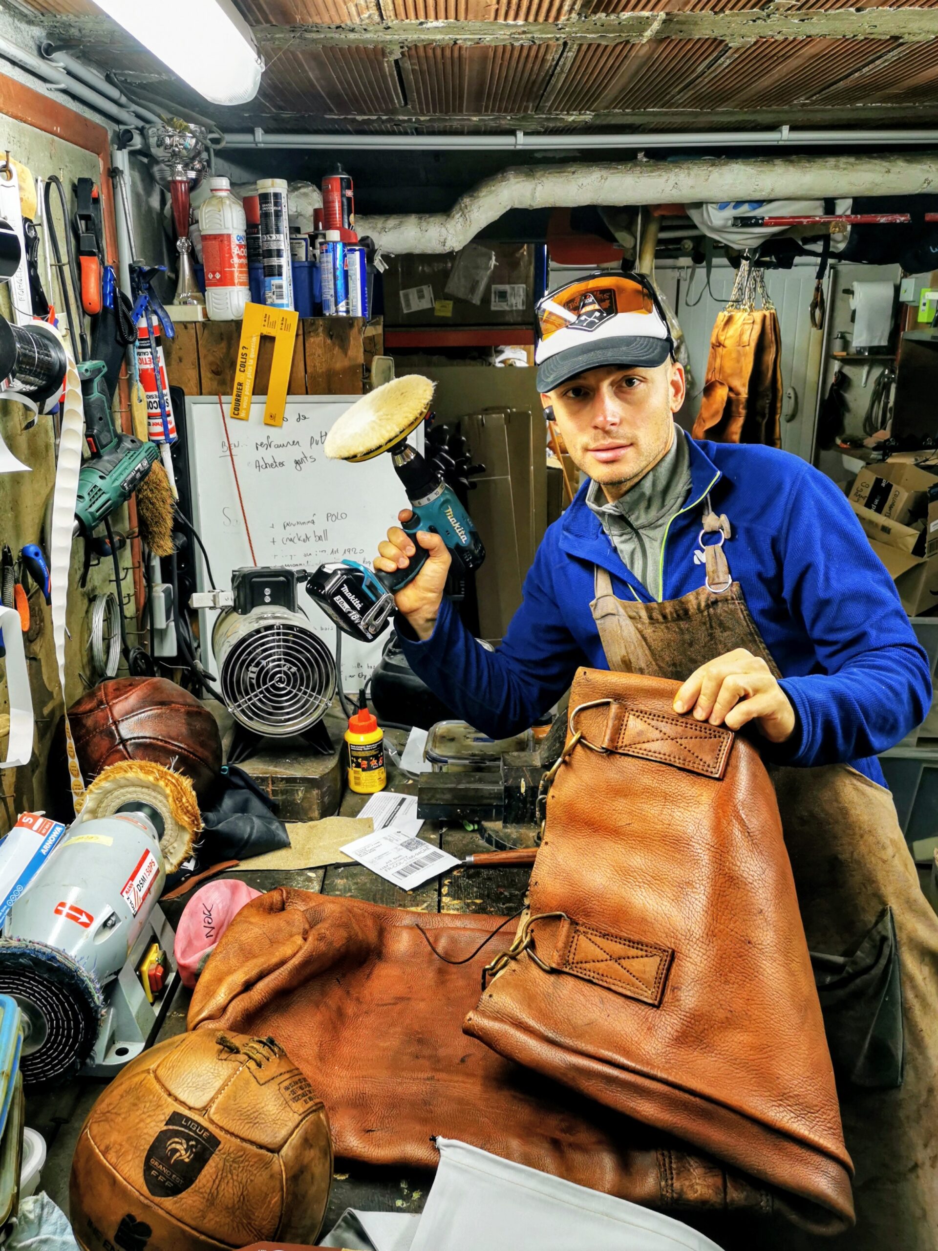 Benjamin Clerget dans son atelier à Audun-le-Roman, avec une polisseuse et des articles de sport anciens en cuir.