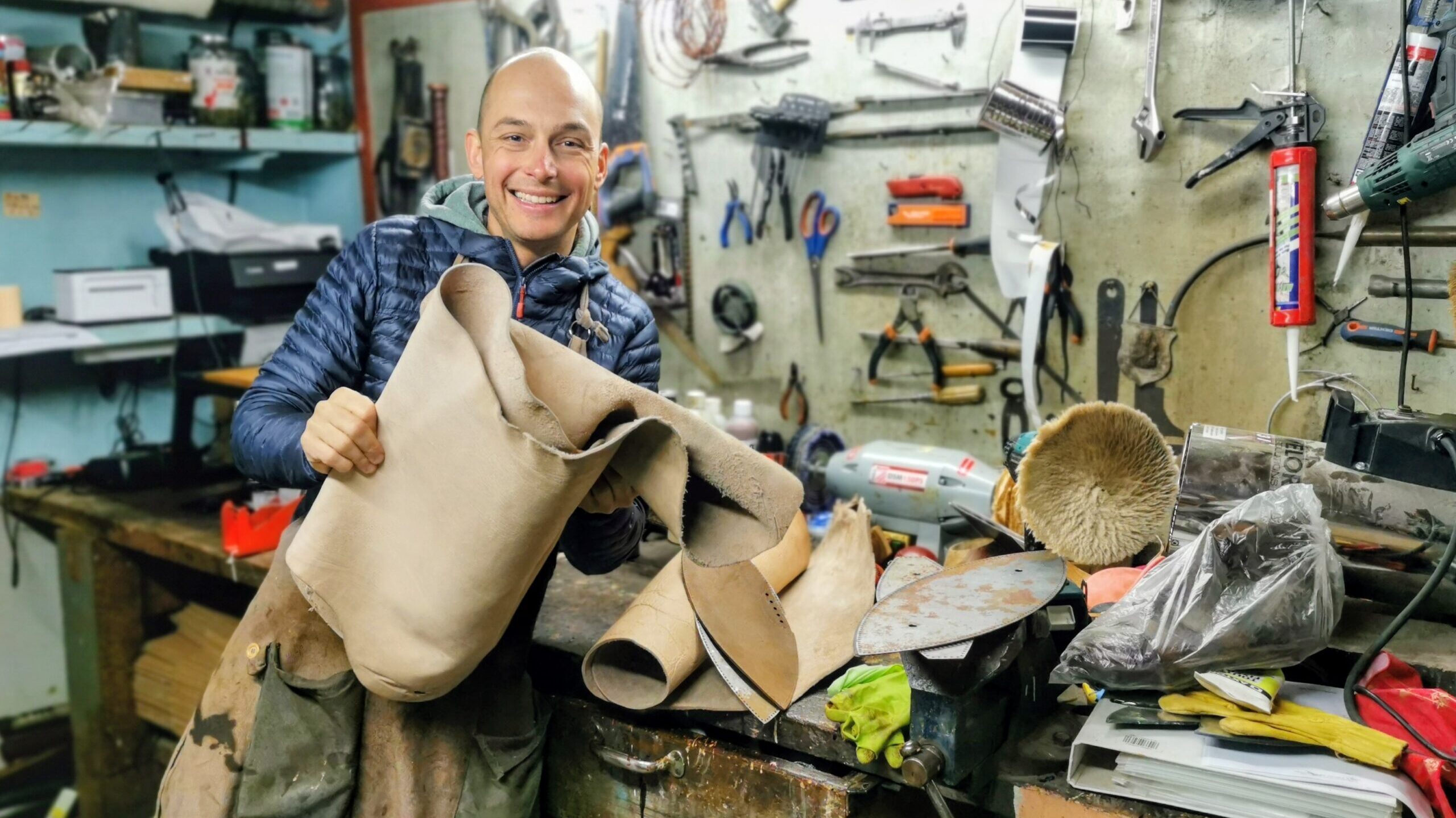 Benjamin Clerget souriant dans son atelier Ben & Flo, tenant une grande pièce de cuir devant son établi.
