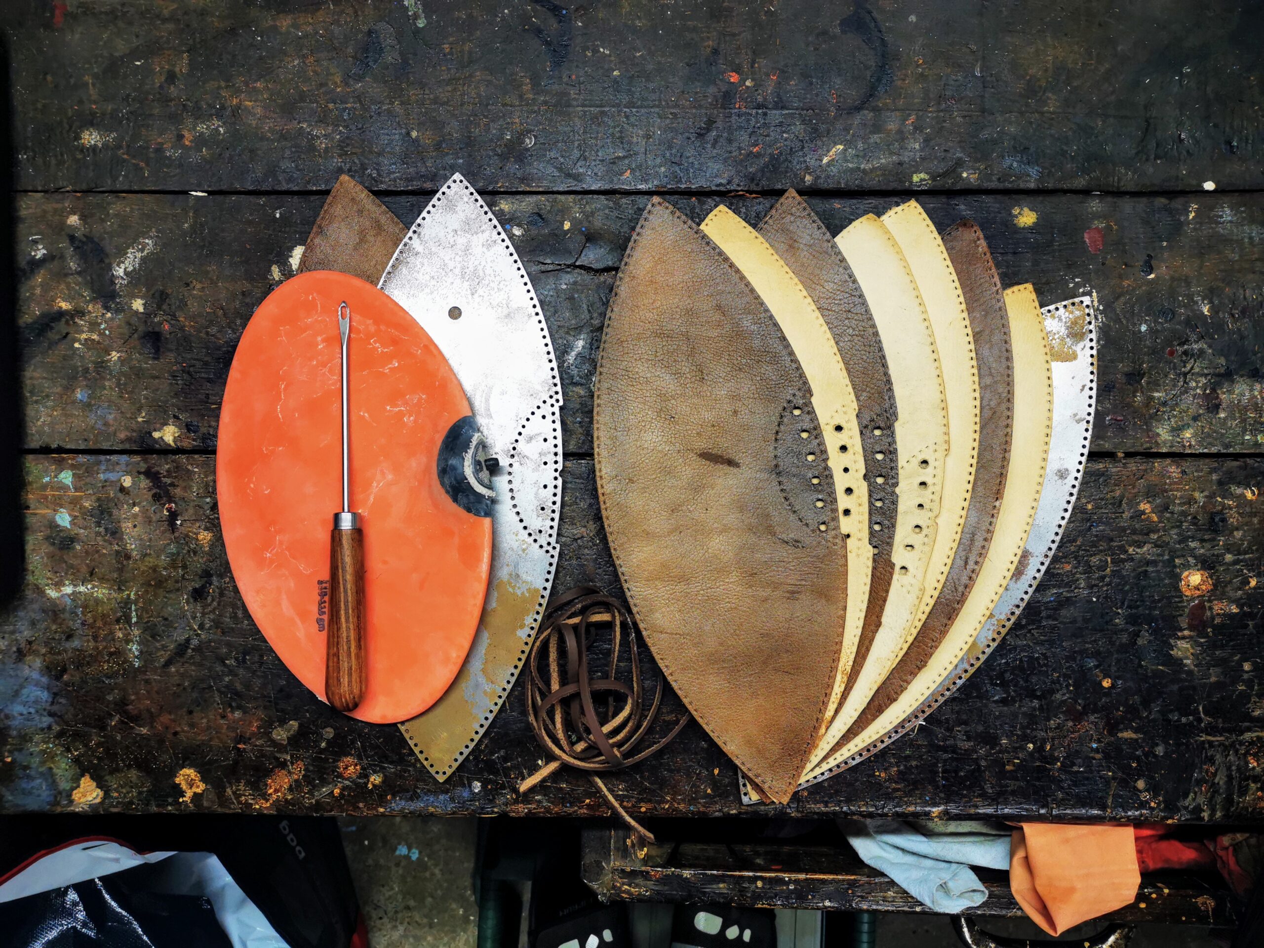 Panneaux de cuir de différentes teintes, découpés et perforés pour fabriquer un ballon de rugby, avec des outils et des lacets.